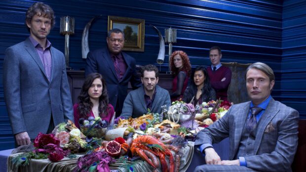 The Hannibal cast is gathered around an elaborate dining table with food and decorations in a dark room, 4K Desktop Wallpaper