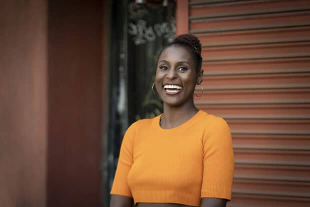 A woman wearing an orange top smiles brightly in front of a textured wall in this insecure tv series wallpaper, HD Desktop Wallpaper