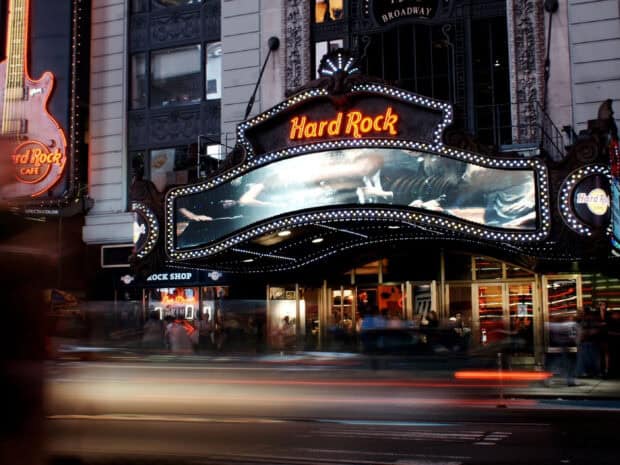 A Hard Rock neon sign glows above a busy city street with light trails and pedestrians, 2K Desktop Wallpaper