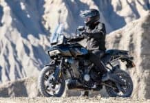 A rider on a Harley Davidson Pan America 1250 motorcycle is parked on rugged terrain with rocky mountains in the background, HD Desktop Wal