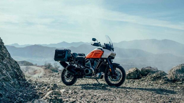 A Harley Davidson Pan America 1250 is parked on rocky terrain with mountains in the background, HD Desktop Wallpaper