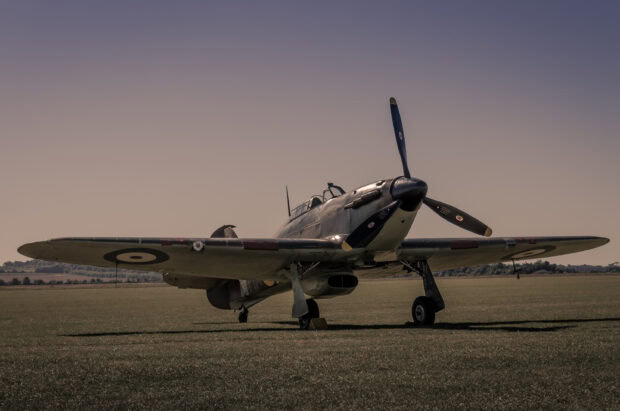 A Hawker Hurricane fighter plane stands on a grass airfield under a clear sky, 2K Desktop Wallpaper