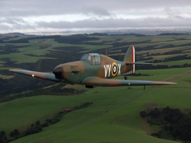 A Hawker Hurricane aircraft flies low over rolling green hills under a cloudy sky, HD Desktop Wallpaper