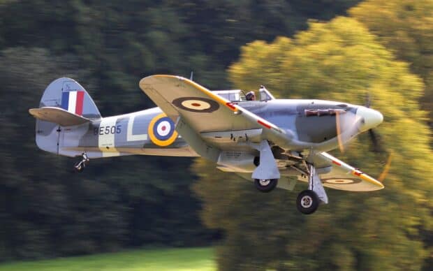 A Hawker Hurricane aircraft flies low with landing gear extended over green fields, 2K Desktop Wallpaper