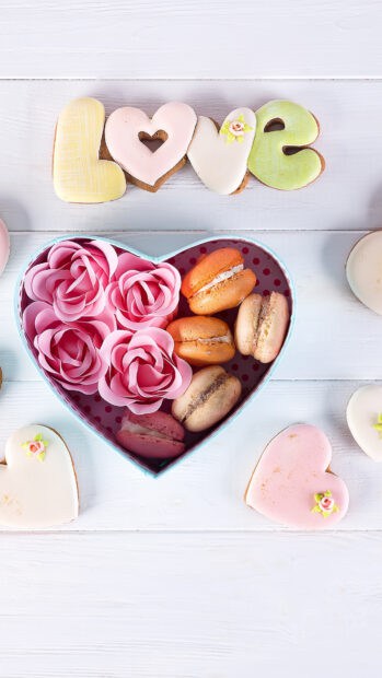 A heart shaped box filled with pink roses and macarons on a white wooden table featuring heart shaped cookies, 4K Phone Wallpaper