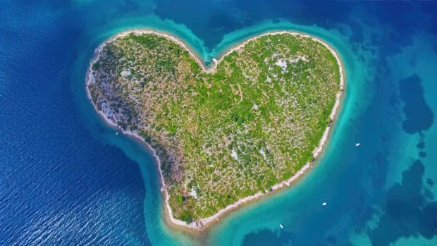 An aerial view of a heart shaped island covered with greenery in the turquoise ocean, 4K Desktop Wallpaper