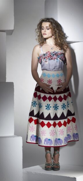 Helena Bonham Carter stands wearing a vibrant patterned dress with floral and elephant motifs, 2K Mobile Wallpaper
