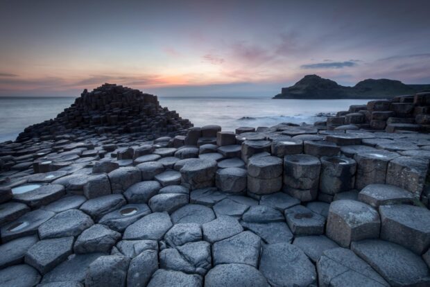 The Giants Causeway shows unique hexagonal rock formations meeting the calm sea in the sunset light, HD Desktop Wallpaper