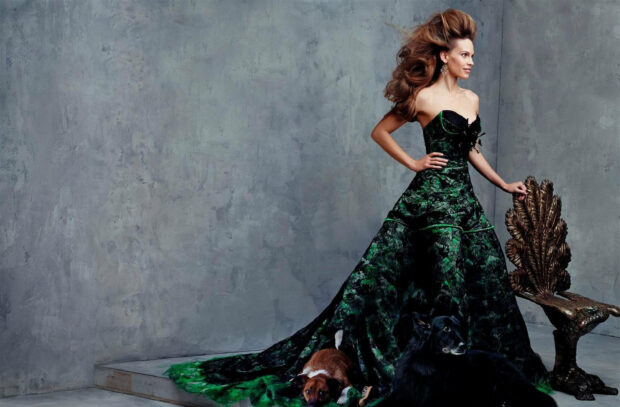 Hilary Swank wears a stunning green gown standing beside two dogs and a decorative chair, HD Desktop Wallpaper