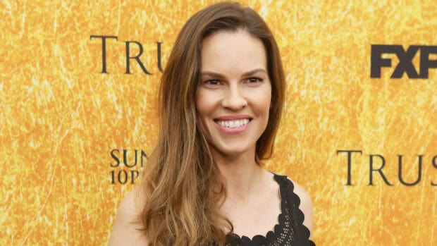 Hilary Swank is smiling in front of a yellow textured backdrop at an event, HD Desktop Wallpaper