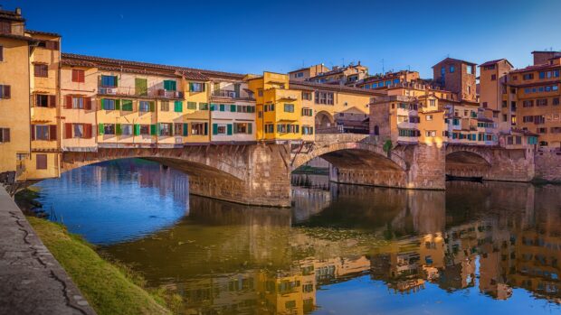 The Ponte Vecchio bridge in Florence reflects beautifully over the river under a clear blue sky, HD Desktop Wallpaper