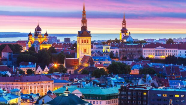 The historic cityscape of Tallinn is beautifully illuminated at sunset with colorful rooftops and church towers, 4K Desktop Wallpaper