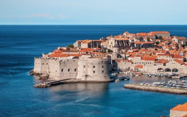The ancient city walls in Dubrovnik surround the coastal town with orange roofs, 2K Desktop Wallpaper