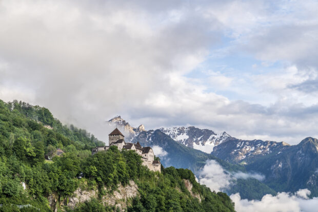 A historic castle stands on a lush green hill surrounded by mountains in Liechtenstein, HD Desktop Wallpaper