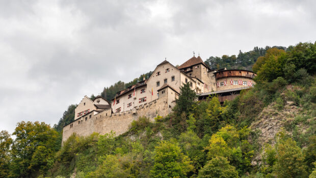 A historic castle stands on a green hill under a cloudy sky in Liechtenstein, 4K Desktop Wallpaper