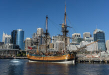 A historic wooden ship is docked in front of modern skyscrapers at the Maritime Museum, HD Desktop Wallpaper