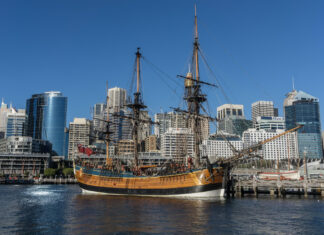 A historic wooden ship is docked in front of modern skyscrapers at the Maritime Museum, HD Desktop Wallpaper
