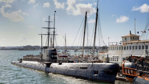 A historic submarine is docked beside sailing ships at the maritime museum harbor, 4K Desktop Wallpaper