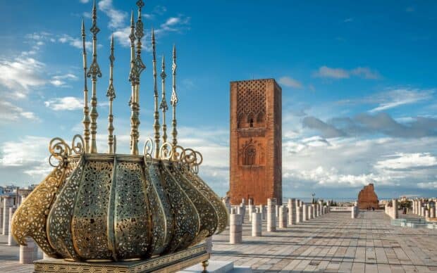 The image shows a historic tower and ornate sculpture under a blue sky in Morocco, HD Desktop Wallpaper