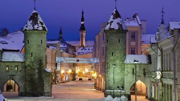 This Estonia city street features historic towers covered in snow during dusk with warm lights, HD Desktop Wallpaper