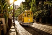 A yellow tram travels through a sunlit street in Rio De Janerio with lush greenery nearby, 2K Desktop Wallpaper