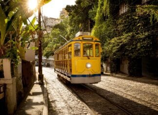 A yellow tram travels through a sunlit street in Rio De Janerio with lush greenery nearby, 2K Desktop Wallpaper