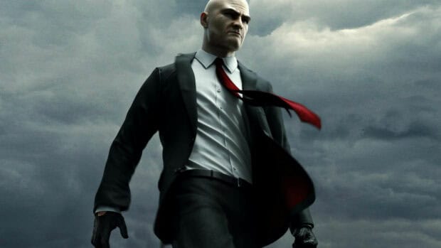 A determined Hitman game character stands against a stormy sky with his red tie flowing, 4K PC Wallpaper