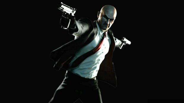 The Hitman character is shown aiming two guns aggressively in a dark setting, HD Desktop Wallpaper