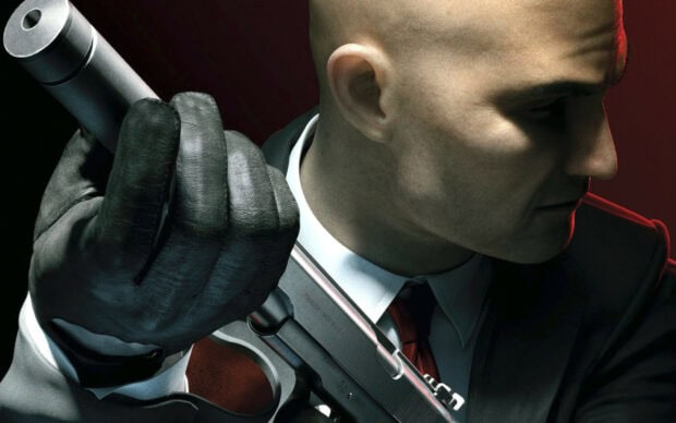 A Hitman Game Wallpapers character in a suit holding a silenced pistol against a dark background, 2K Desktop Wallpaper
