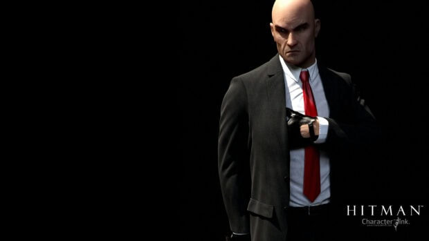 The Hitman character stands confidently wearing a red tie and black gloves in a dark setting, 2K Desktop Wallpaper