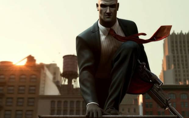 A hitman crouches holding a sniper rifle with a city skyline at sunset in the background, HD Desktop Wallpaper