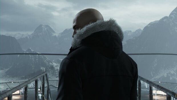A bald man in a fur lined hooded jacket stands on a platform overlooking snowy mountains in Hitman game, 4K Desktop Wallpaper