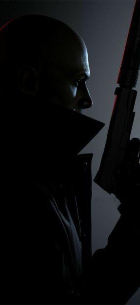 A Hitman from the game holding a silenced pistol in a dark setting, 2K Phone Wallpaper