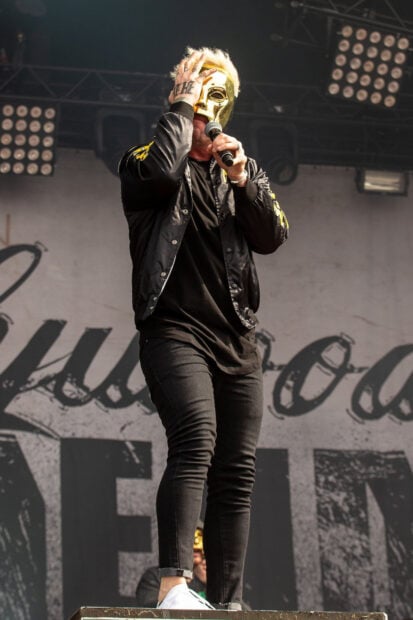 A member of Hollywood Undead band wearing a gold mask and singing on stage during a concert, HD Mobile Wallpaper