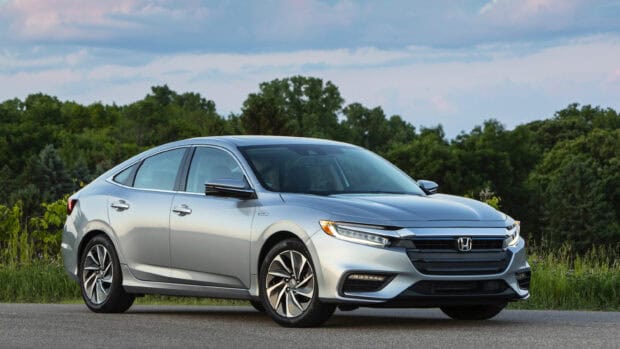 A silver Honda Insight is parked on the road with green trees and a cloudy sky in the background, 2K Desktop Wallpaper