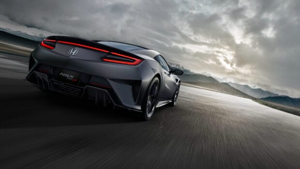 A sleek Honda NSX driving fast on an open road with mountains and cloudy sky, 4K Desktop Wallpaper