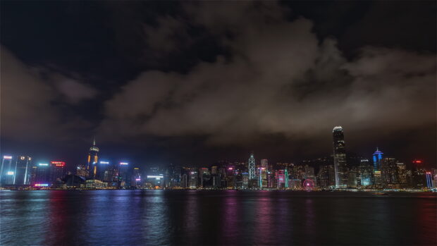 The Hong Kong skyline reflects colorful lights on the water under a cloudy night sky, 4K Desktop Wallpaper
