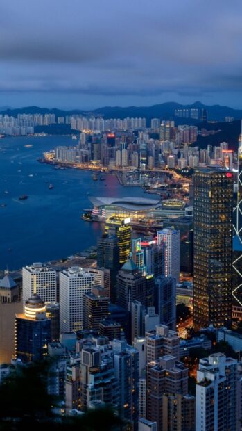 The Hong Kong skyline is beautifully illuminated during dusk with vibrant city lights reflecting on the water, HD Mobile Wallpaper
