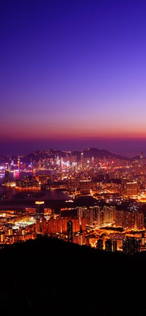 The Hong Kong skyline glows brightly under a twilight sky with vibrant city lights, 2K Mobile Wallpaper