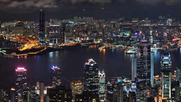 The Hong Kong skyline at night displays illuminated buildings reflecting over the water, HD Desktop Wallpaper