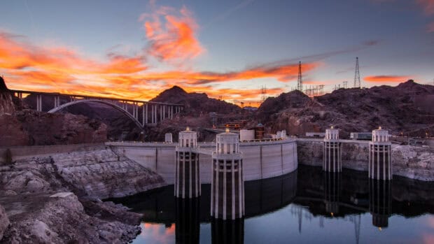 The Hoover Dam reflects in the calm water with vibrant sunset clouds, 4K Desktop Wallpaper