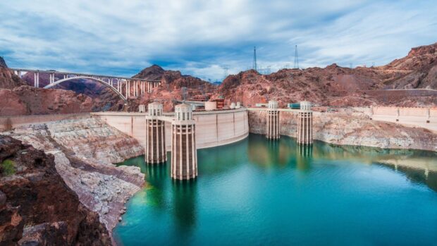 The Hoover Dam is shown with blue water and rocky surroundings under a cloudy sky, HD Desktop Wallpaper