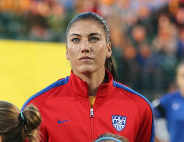 Hope Solo is seen wearing a red jacket with USA emblem and looking ahead during the game, HD Desktop Wallpaper