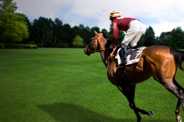A jockey rides a brown horse on a lush green field during horse racing, 2K Desktop Wallpaper