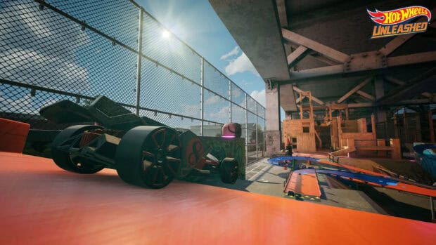 A Hot Wheels car is positioned on an orange racing track near a fenced urban skate park, HD Desktop Wallpaper