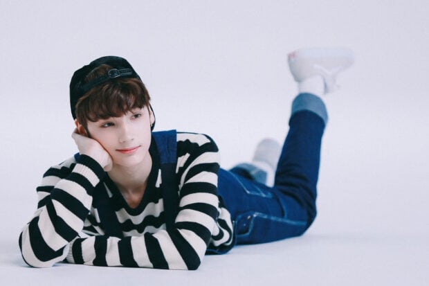 Huening Kai is lying down wearing a casual striped sweater and jeans in this photo, HD Desktop Wallpaper