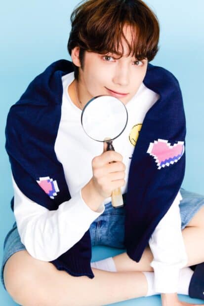 A young man named Huening Kai holding a magnifying glass while sitting cross legged, HD Phone Wallpaper