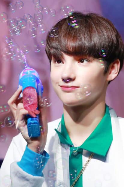 Huening Kai is playing with a bubble gun surrounded by floating bubbles, HD Mobile Wallpaper