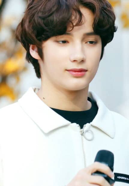 A close up of Huening Kai holding a microphone in a white jacket, HD Phone Wallpaper