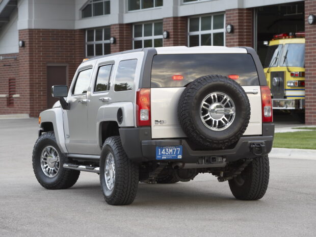 A silver Hummer H3 is parked next to a fire station with its rear spare tire visible, HD Desktop Wallpaper